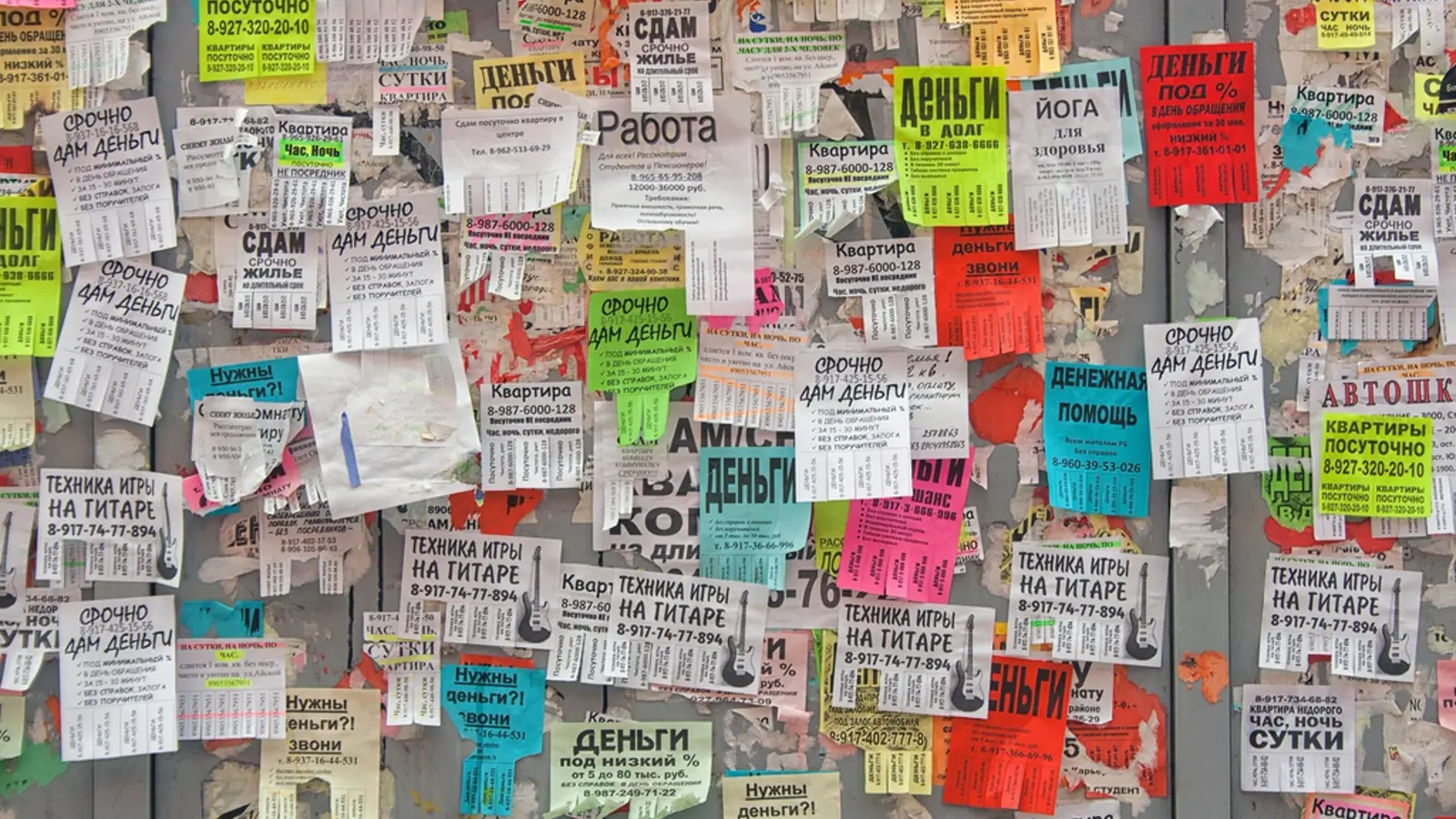 A public notice board covered in hundreds of overlapping paper flyers, many pasted on top of each other