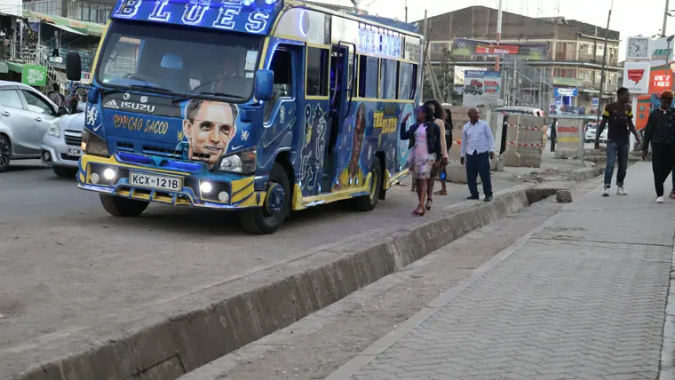A decorated matatu on a Nairobi street, with roadside kiosks and painted signage behind it