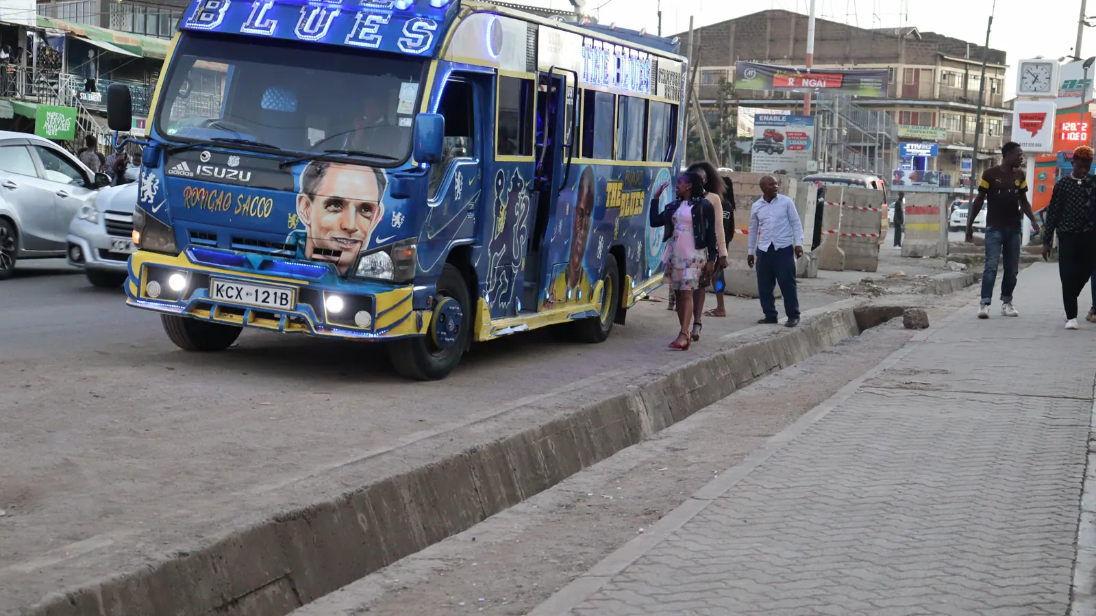A decorated matatu on a Nairobi street, with roadside kiosks and painted signage behind it