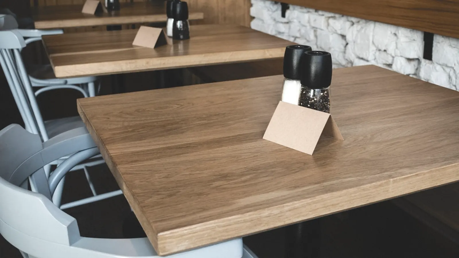 Bare restaurant tables set with wooden table tents and condiment holders